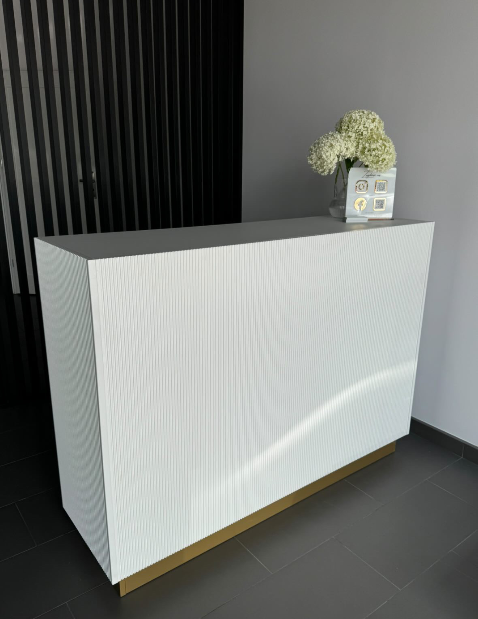 Eine stilvolle Empfangstheke für das Wohnzimmer – Empfangsmöbel mit geriffelter Front in Beige und goldenen Akzenten. Eine stilvolle Empfangstheke für das Wohnzimmer – Empfangsmöbel mit geriffelter Front in Beige und goldenen Akzenten.